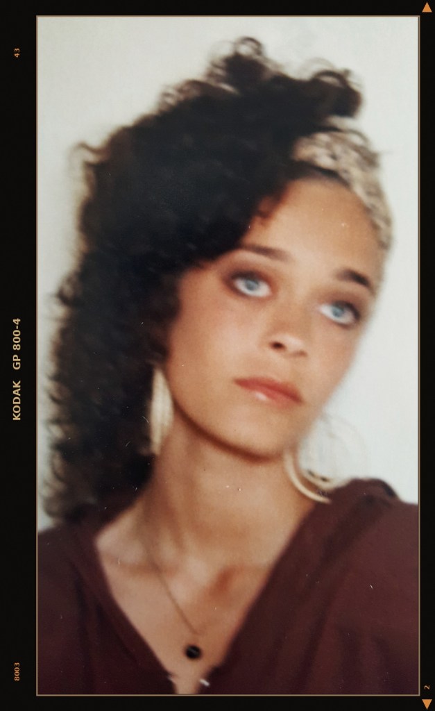 "Kodak-framed vintage portrait of a young woman, around seventeen, dark curly hair, hoop earrings, maroon top." Zavet 1.0.1